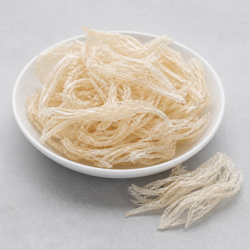 Dried edible bird's nest strands in a shallow white dish beside loose pale ivory fibrous threads